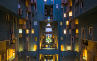Night-lit geometric courtyard of Ricardo Bofill architecture – golden windows glowing within a symmetrical blue facade