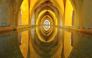 Golden tunnel with concentric arches and reflective floor – symmetrical interior design with dramatic lighting