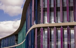 Colorful vertical facade of contemporary building – sleek design with purple and teal tones under soft daylight