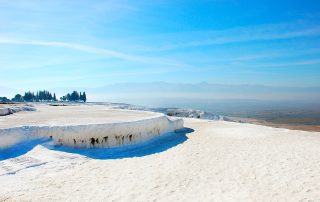 Bright white terraces and blue thermal pools of Pamukkale under clear sky