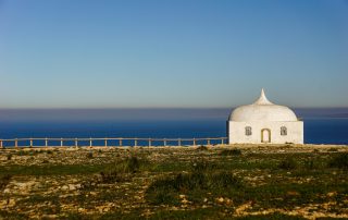 Small white chapel near the coast with blue ocean backdrop – peaceful seaside religious landmark
