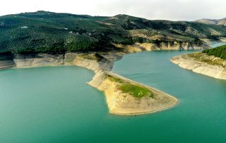 Curved shoreline of green hills by turquoise reservoir – aerial view of Embalse de Zahara-El Gastor, Andalusia