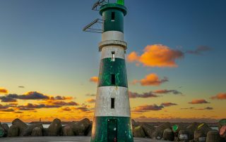 Striped lighthouse by the ocean at sunset – maritime beacon against vibrant evening colors
