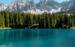 Turquoise lake with alpine forest and snowy mountains under clear blue sky